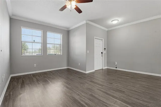 an empty room with wooden floor chandelier fan and windows