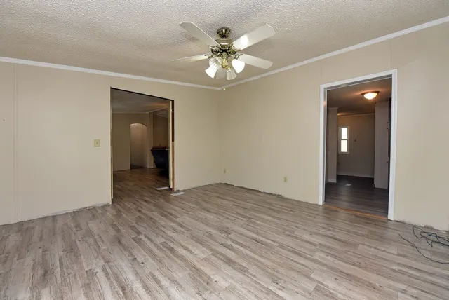 a view of an empty room with wooden floor and a ceiling fan