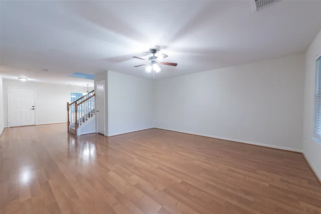 a view of an empty room with wooden floor and a ceiling fan