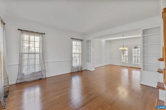 an empty room with wooden floor and windows with curtains