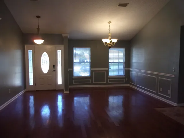 an empty room with wooden floor chandelier and windows