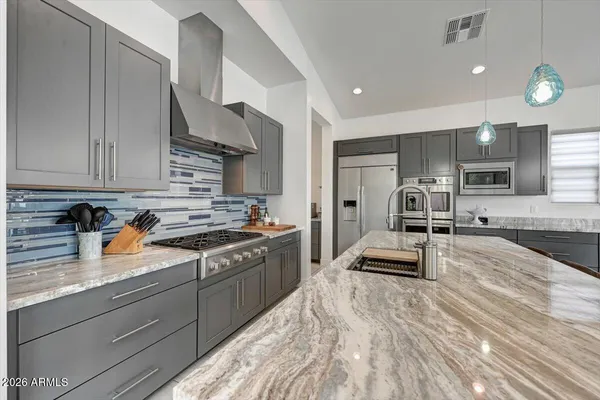 a large kitchen with stainless steel appliances granite countertop a stove a sink a refrigerator and white cabinets with wooden floor