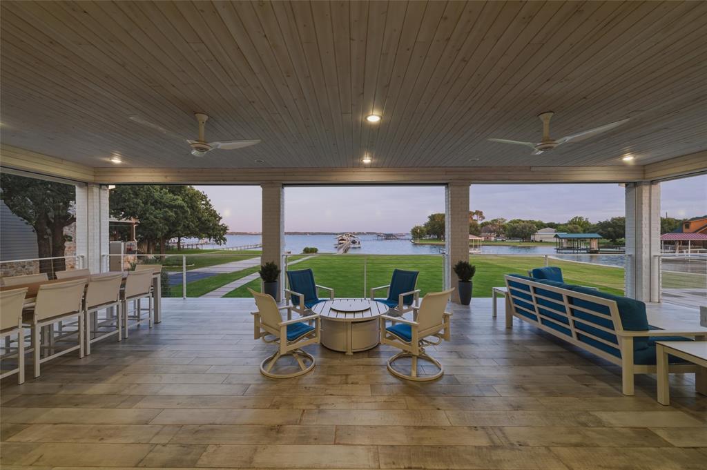 6625 Sandy Beach Road Azle, TX 76020 - Photo 24 of 40 Covered patio features painted brick support columns, recessed lighting, mounted ceiling fans, cable railing detail, and large-format tile flooring throughout the outdoor living area. Open layout overlooks the lawn spaces, private dock access, and surrounding waterfront views.