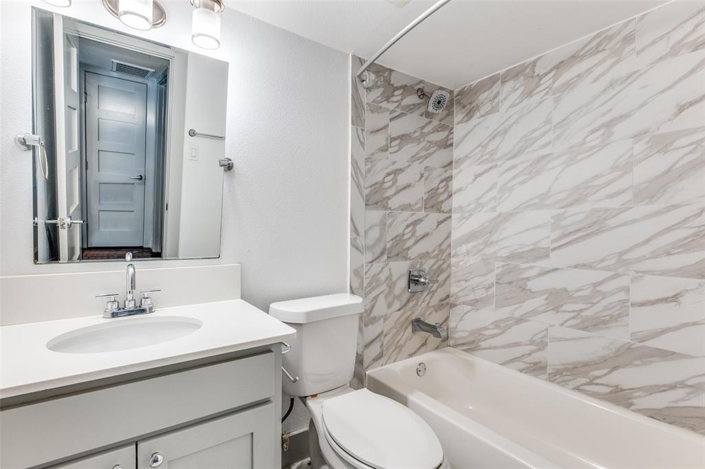 4633 Fairmount Street, Unit 109 Dallas, TX 75219 - Photo 14 of 14 Bathroom featuring a vanity with a white countertop and undermount sink, a toilet, and a bathtub with a shower surround tiled in a white and gray marble-look pattern