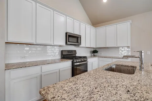 a kitchen with granite countertop a sink a stove top oven and cabinetry