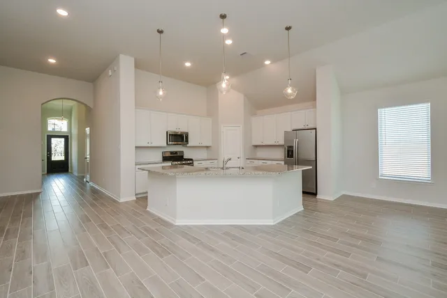 a large kitchen with stainless steel appliances kitchen island wooden floors and white cabinets