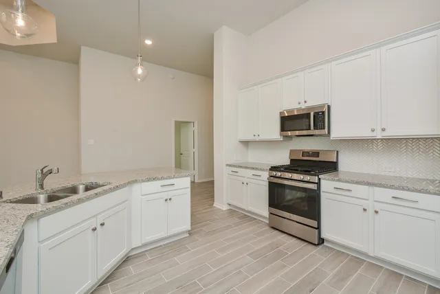 a large white kitchen with stainless steel appliances granite countertop a stove a sink dishwasher and a microwave oven with white cabinets