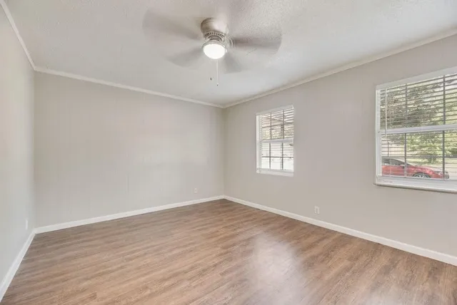 an empty room with wooden floor fan and windows