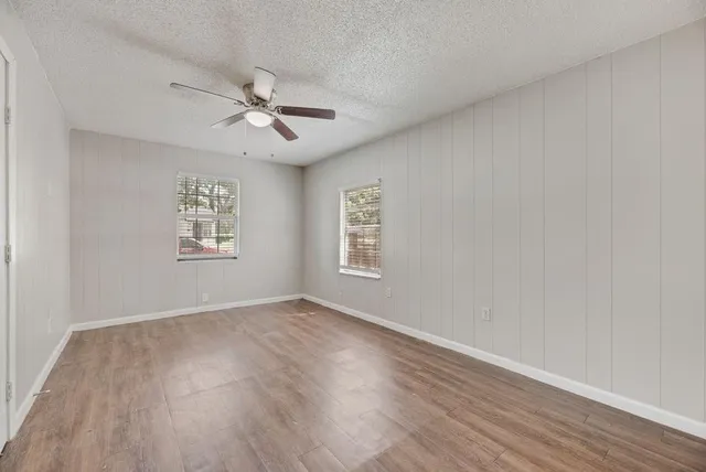 an empty room with wooden floor ceiling fan and windows
