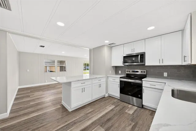 a kitchen with stainless steel appliances granite countertop a stove top oven a sink dishwasher and a refrigerator with wooden floor