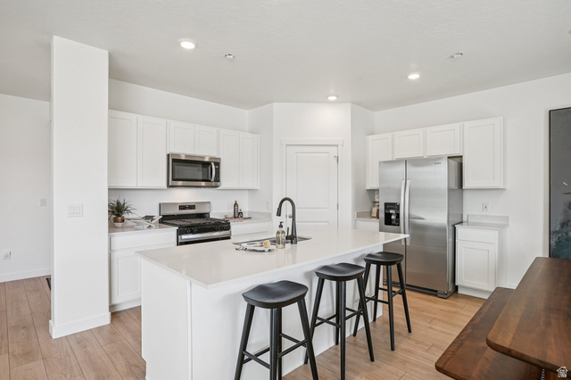 2097 North Ostler Peak Road, Unit 115 Heber City, UT 84032 - Photo 29 of 33 Kitchen featuring a central island with countertop seating, white shaker cabinetry, stainless steel appliances, and light wood-finish flooring