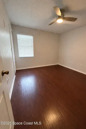 an empty room with wooden floor fan and windows