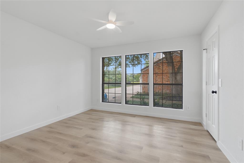 17118 Planters Row Addison, TX 75001 - Photo 12 of 18 Bright room featuring three large multi-pane windows, wood-finish flooring, a contemporary ceiling fan with integrated lighting, white baseboards, and a paneled door with black hardware