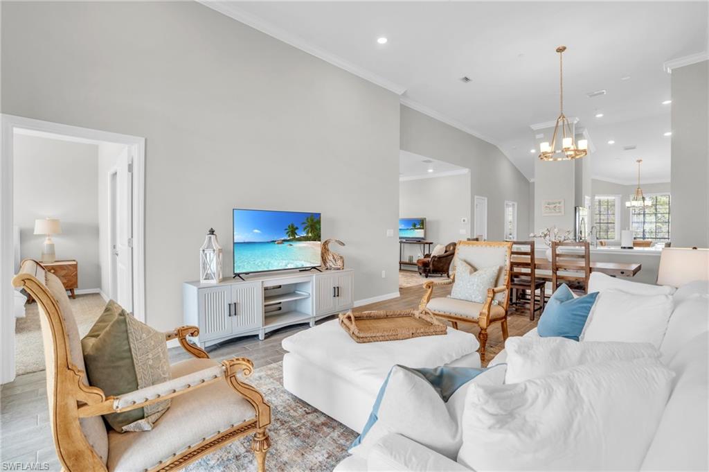 11761 Venetian Lagoon Drive, Unit 204 Fort Myers, FL 33913 - Photo 11 of 46 Living room with baseboards, an inviting chandelier, light wood-style flooring, lofted ceiling, and ornamental molding