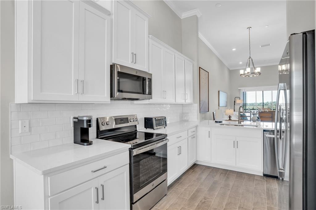 11761 Venetian Lagoon Drive, Unit 204 Fort Myers, FL 33913 - Photo 4 of 46 Kitchen with backsplash, crown molding, a chandelier, appliances with stainless steel finishes, and a sink