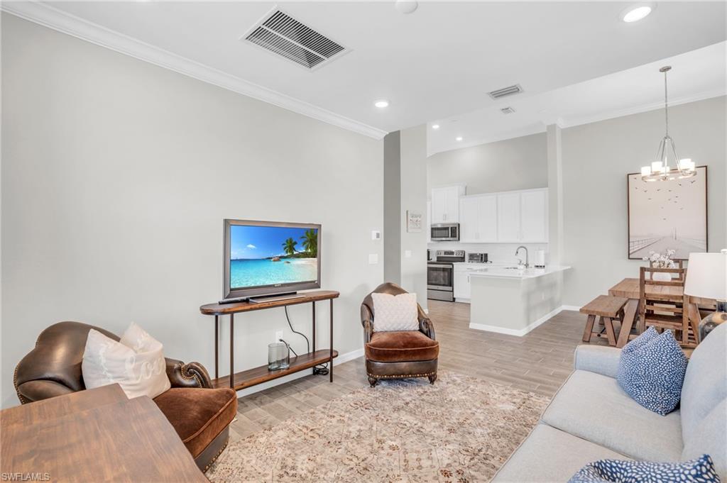 11761 Venetian Lagoon Drive, Unit 204 Fort Myers, FL 33913 - Photo 7 of 46 Living area featuring visible vents, crown molding, baseboards, a chandelier, and light wood-type flooring
