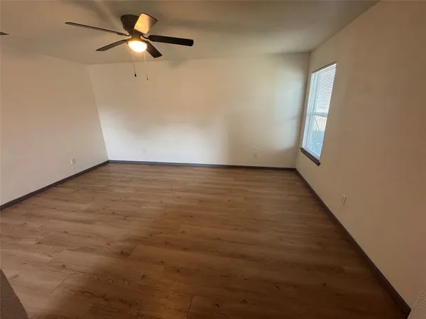 an empty room with wooden floor fan and windows