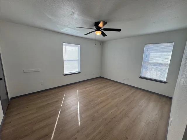 an empty room with wooden floor fan and windows