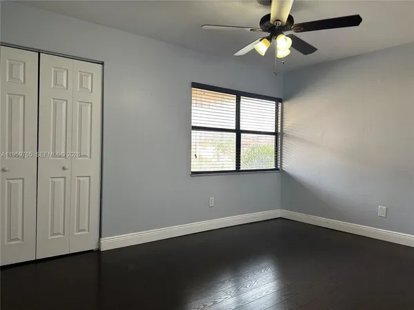 an empty room with wooden floor chandelier fan and windows