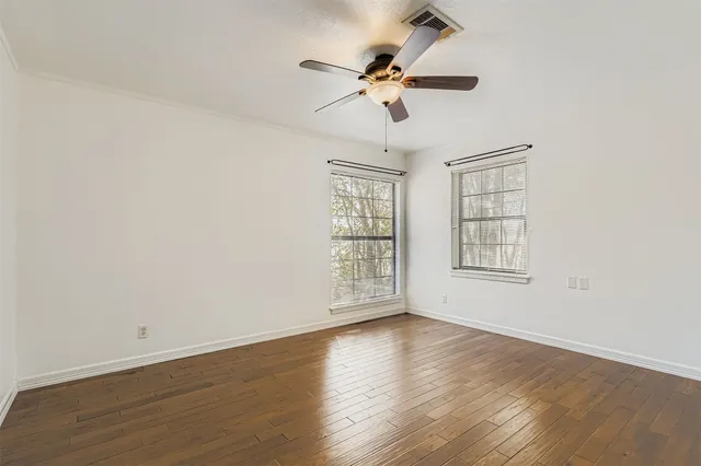an empty room with wooden floor fan and windows