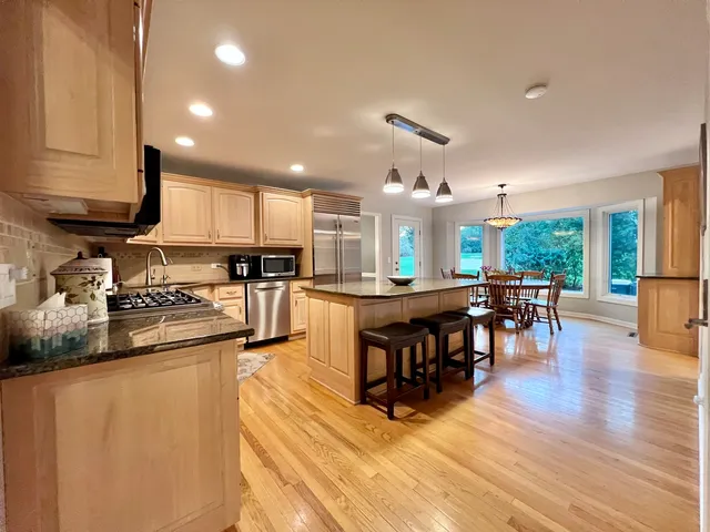 a kitchen with stainless steel appliances granite countertop a stove top oven a sink a dining table and chairs with wooden floor