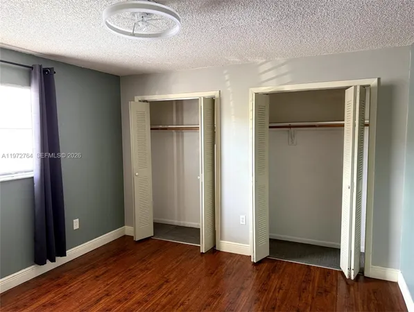 an empty room with wooden floor closet and windows