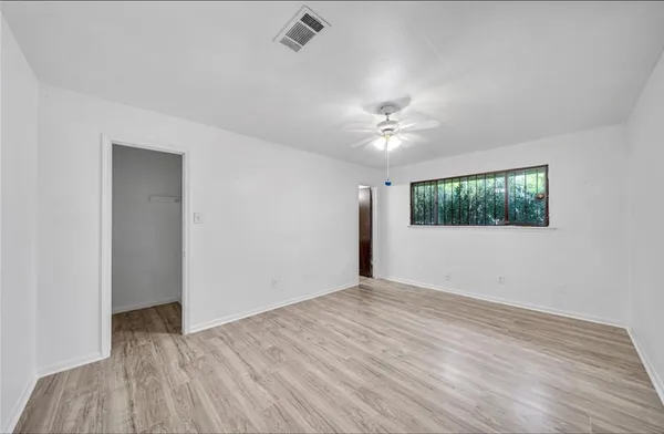 a view of an empty room with wooden floor and a ceiling fan