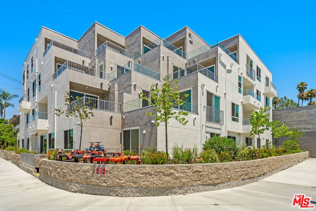 a view of a white building among the street with flower plants