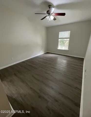 an empty room with wooden floor ceiling fan and windows