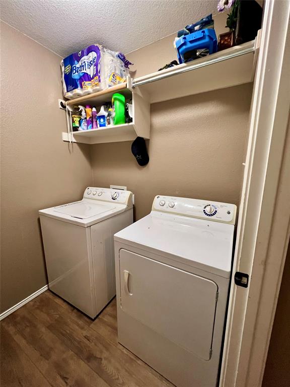 12201 Rolling Ridge Drive Fort Worth, TX 76028 - Photo 18 of 21 Dedicated laundry area featuring wood-finish flooring, a white top-load washing machine, a white front-load dryer, and wall-mounted shelving for storage
