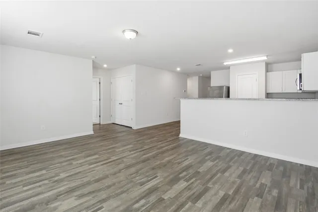 an empty room with wooden floor and kitchen view