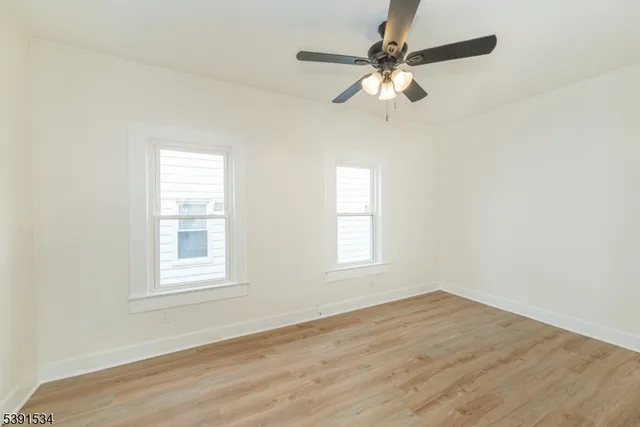 an empty room with wooden floor fan and windows