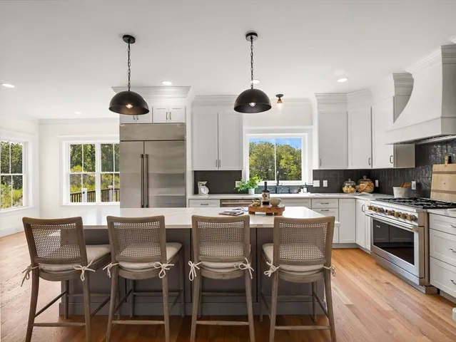 a kitchen with stainless steel appliances granite countertop a stove top oven a sink a dining table and chairs with wooden floor