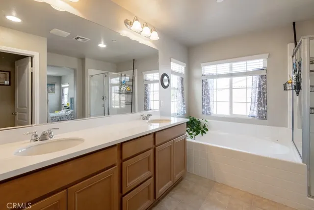 a bathroom with a granite countertop double vanity sink a large mirror a bathtub and next to a window