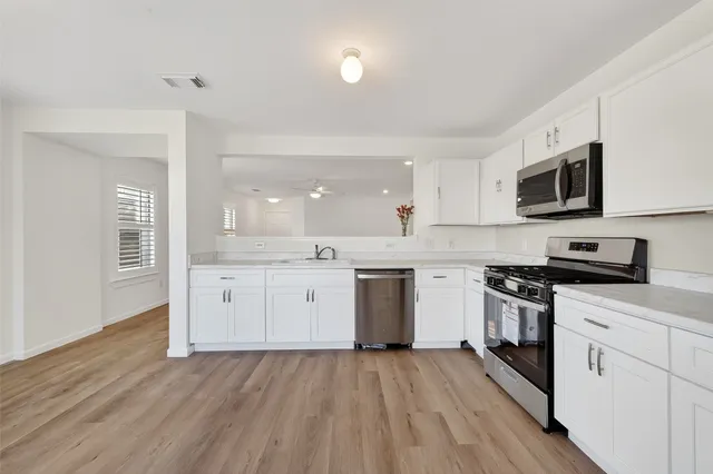 a kitchen with stainless steel appliances granite countertop a stove top oven a sink dishwasher and a microwave oven with white cabinets