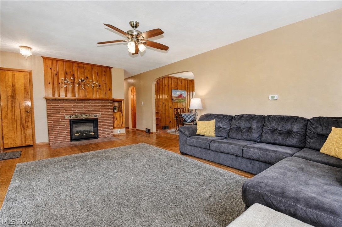 3864 State Road South Ashtabula, OH 44004 - Photo 9 of 50 Hardwood flooring, brick fireplace with mantel, paneled accent wall, arched doorway, and ceiling fan with lighting