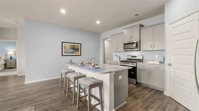 a kitchen with stainless steel appliances granite countertop a stove top oven a sink dishwasher and a refrigerator with wooden floor