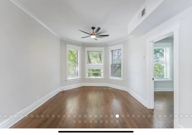 an empty room with wooden floor chandelier fan and windows