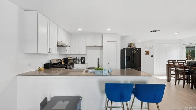 a kitchen with stainless steel appliances a dining table chairs refrigerator and sink