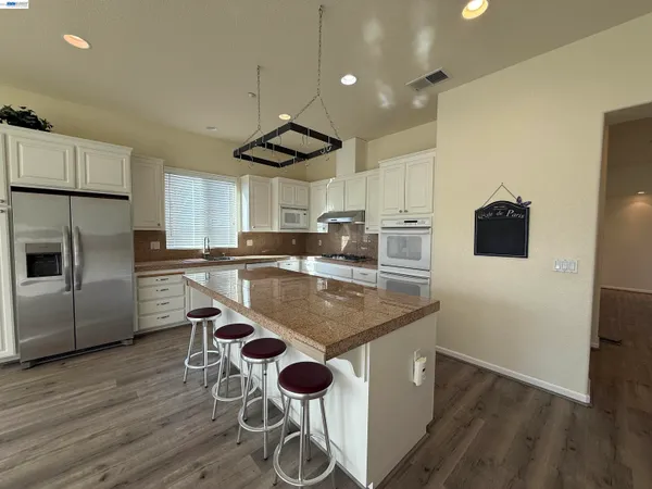 a kitchen with stainless steel appliances granite countertop a sink a stove a refrigerator and island with wooden floor