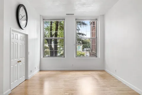 a view of an empty room with a window and wooden floor