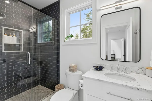 a bathroom with a granite countertop toilet a sink a mirror and shower