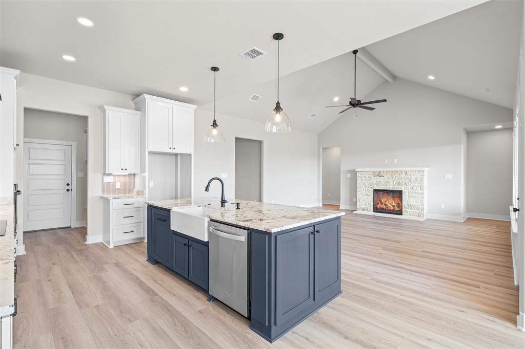 900 Day Star Drive Hewitt, TX 76643 - Photo 16 of 40 Kitchen featuring white cabinets, hanging light fixtures, a stone fireplace, a center island with sink, and light wood-style flooring