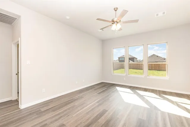 an empty room with wooden floor fan and windows
