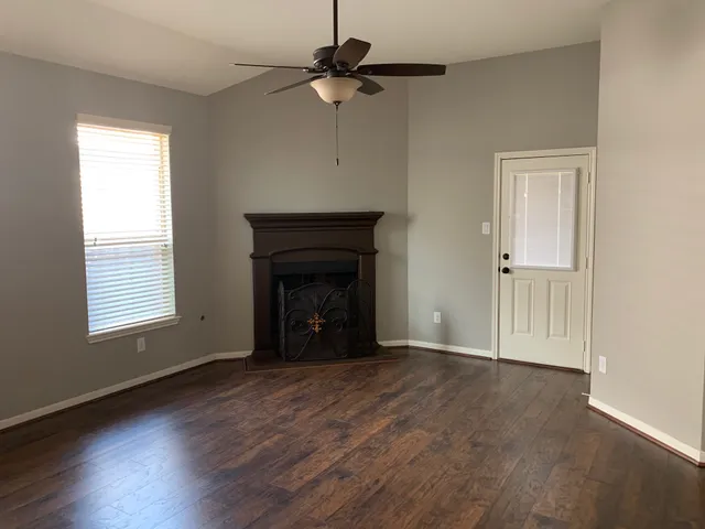 an empty room with wooden floor a ceiling fan and windows