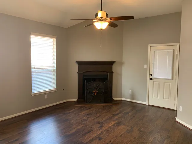 an empty room with wooden floor a chandelier fan and a fireplace