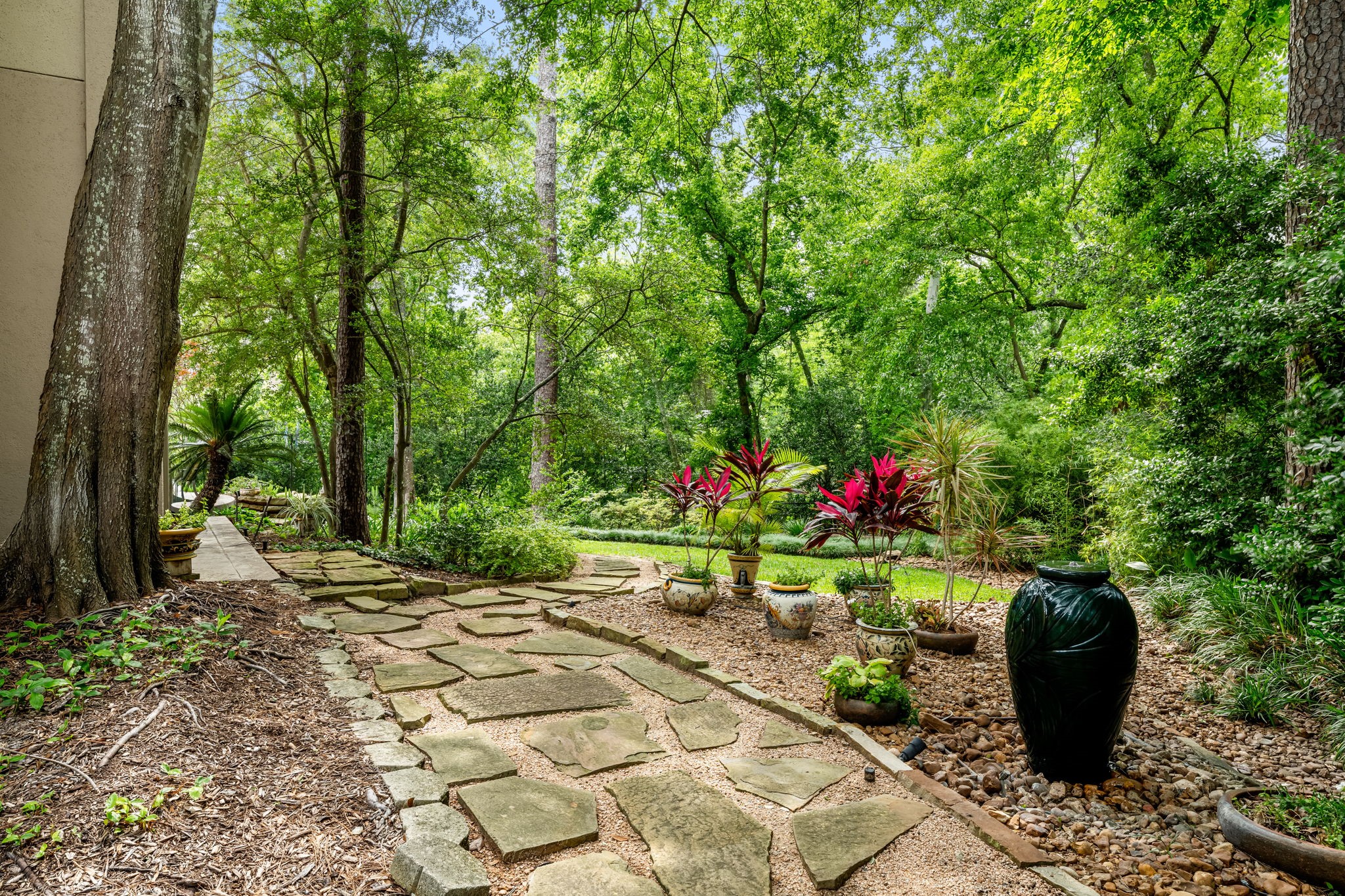 6 Mott Lane Houston, TX 77024 - Photo 50 of 50 Serene garden pathway with natural stone pavers, surrounded by lush, mature trees and vibrant landscaping, creating a peaceful park-like setting perfect for quiet strolls or relaxation.