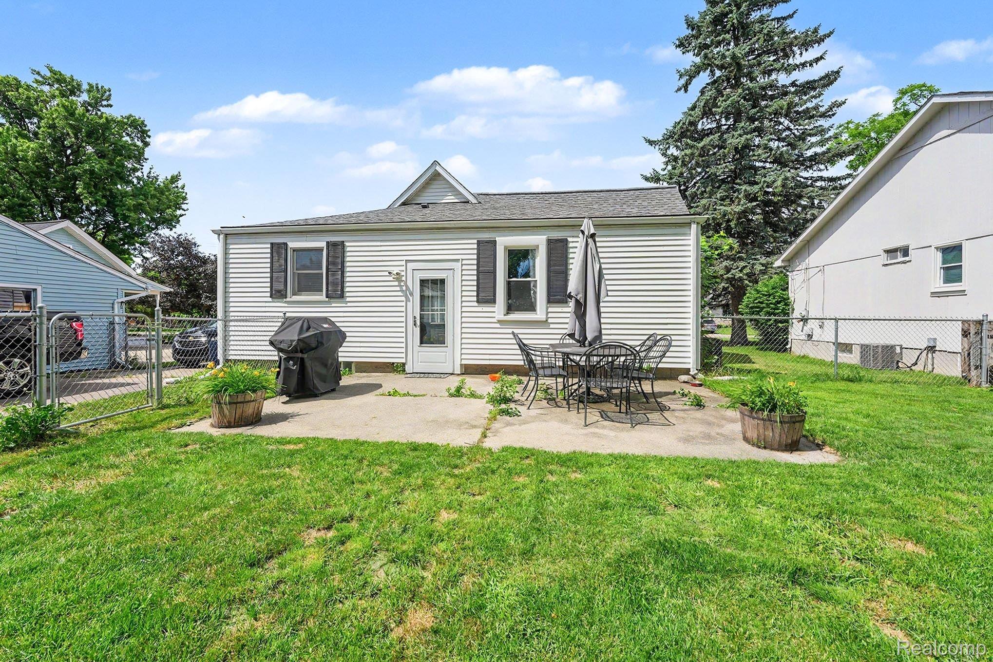 8215 Clinton River Road Sterling Heights, MI 48314 - Photo 25 of 28 Rear exterior with white siding and dark louvered shutters, featuring a concrete patio and a lush green lawn