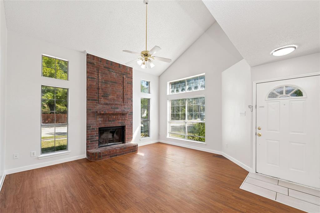 3721 Smartt Street Rowlett, TX 75088 - Photo 3 of 25 Unfurnished living room with high vaulted ceiling, wood finished floors, a textured ceiling, a ceiling fan, and a brick fireplace