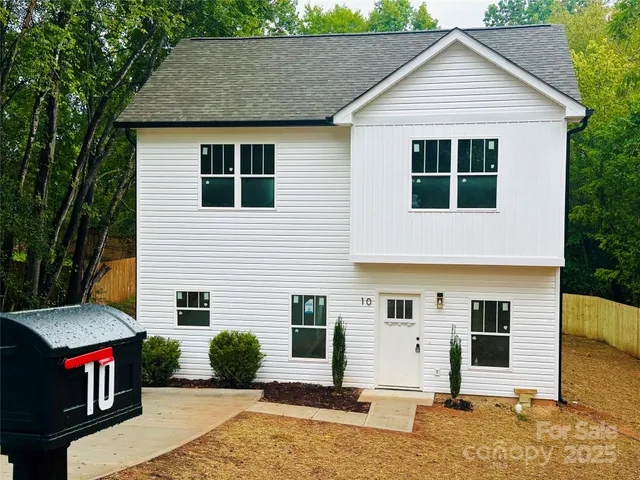 a view of a white house with a small yard plants and large tree